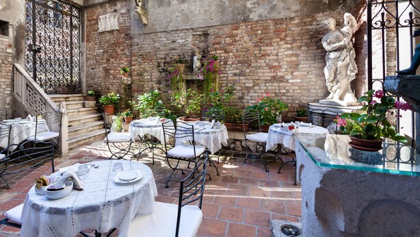 Eine Außenpatio-Terrasse mit runden Tischen und Stühlen, Topfpflanzen und einer Statue.