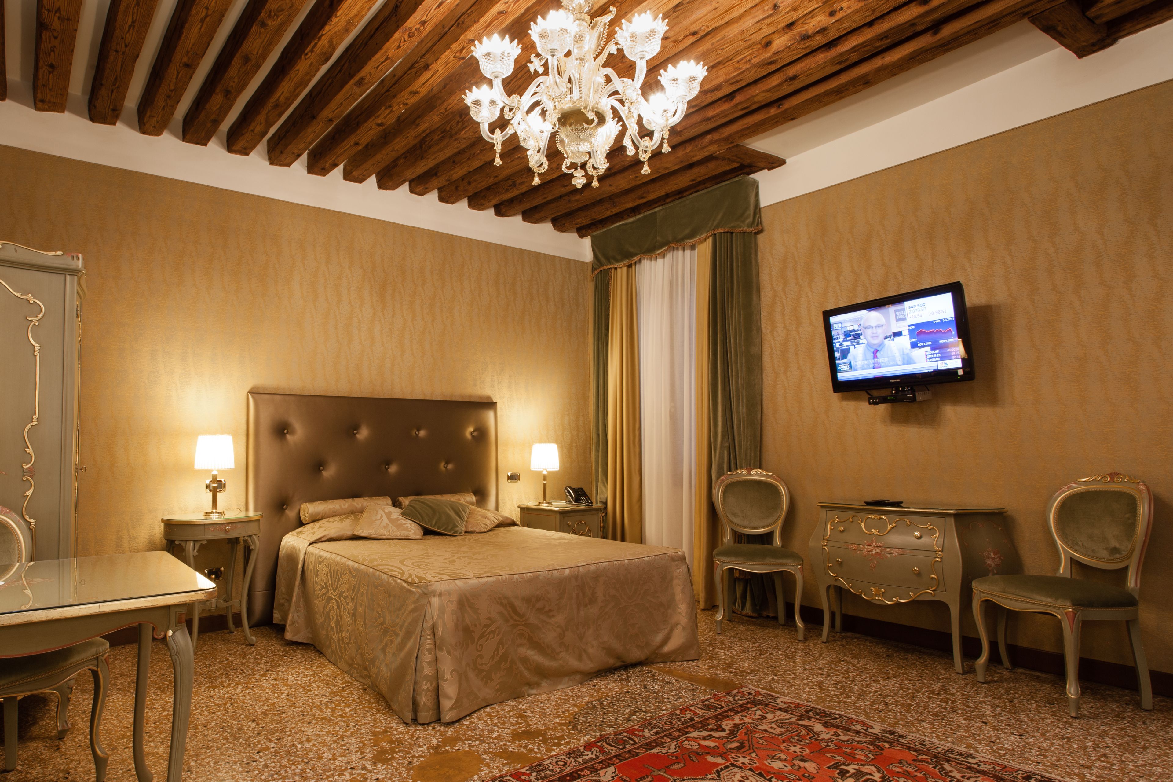 A hotel room with a large bed, two bedside tables with lamps, a television mounted on the wall, and a wooden ceiling.