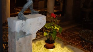 Eine Statue auf einem Sockel, eine Topfpflanze und ein Raum mit Schachbrettfußboden und Säulen.