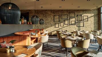 Interior moderno de restaurante con pared decorada, varias mesas para comer y diferentes opciones de asientos, incluyendo un sofá y sillas.