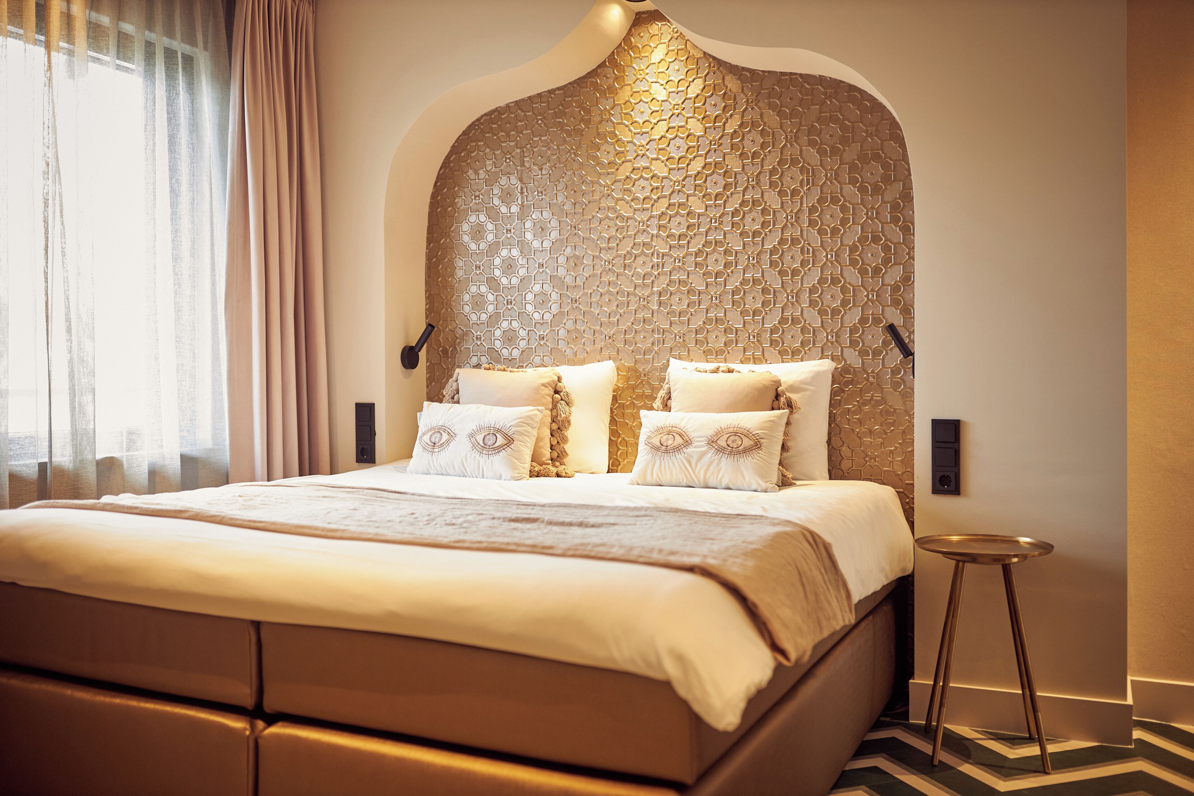 A modern hotel room with a large bed, a decorative wall, and a small side table.