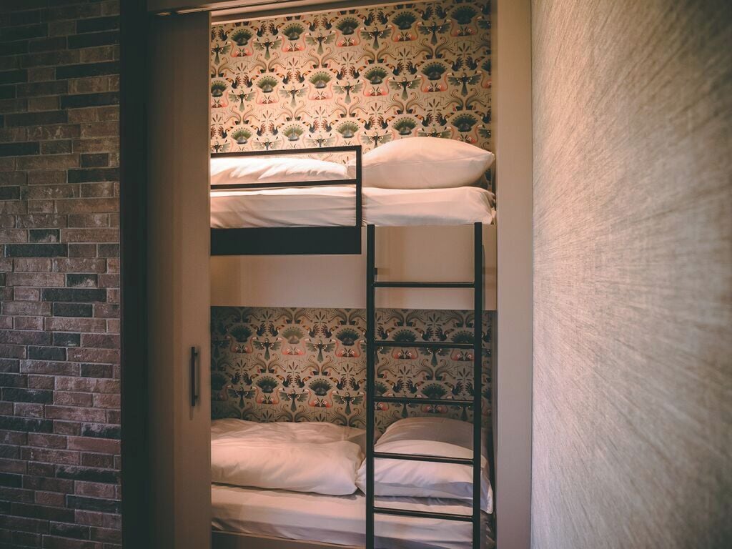 Ein Schlafzimmer mit Etagenbetten, einer Ziegelwand und ornamentalem Wandpapier.