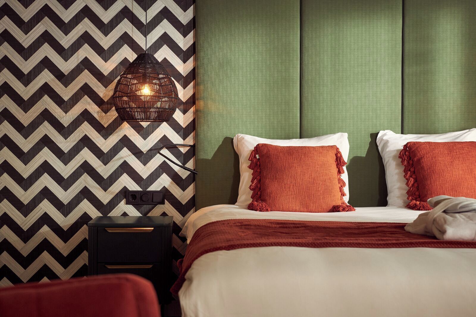 A hotel room with a bed, a nightstand, a lamp, and a patterned wall.