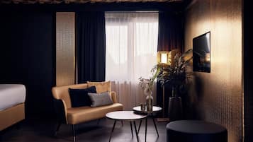 A modern hotel room with a sofa, two small tables, a lamp, and a potted plant.