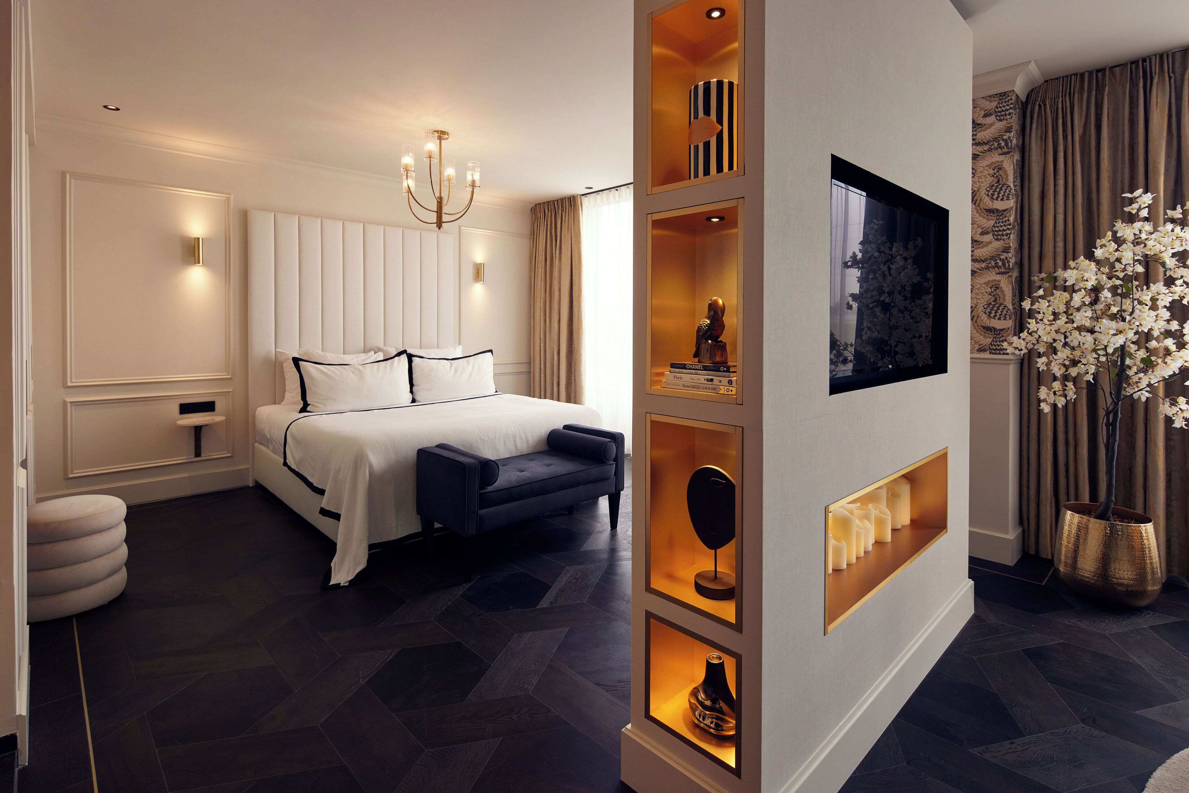 Une chambre moderne avec un grand lit, des tables de chevet, un téléviseur fixé au mur et une étagère décorative ornée de bougies.