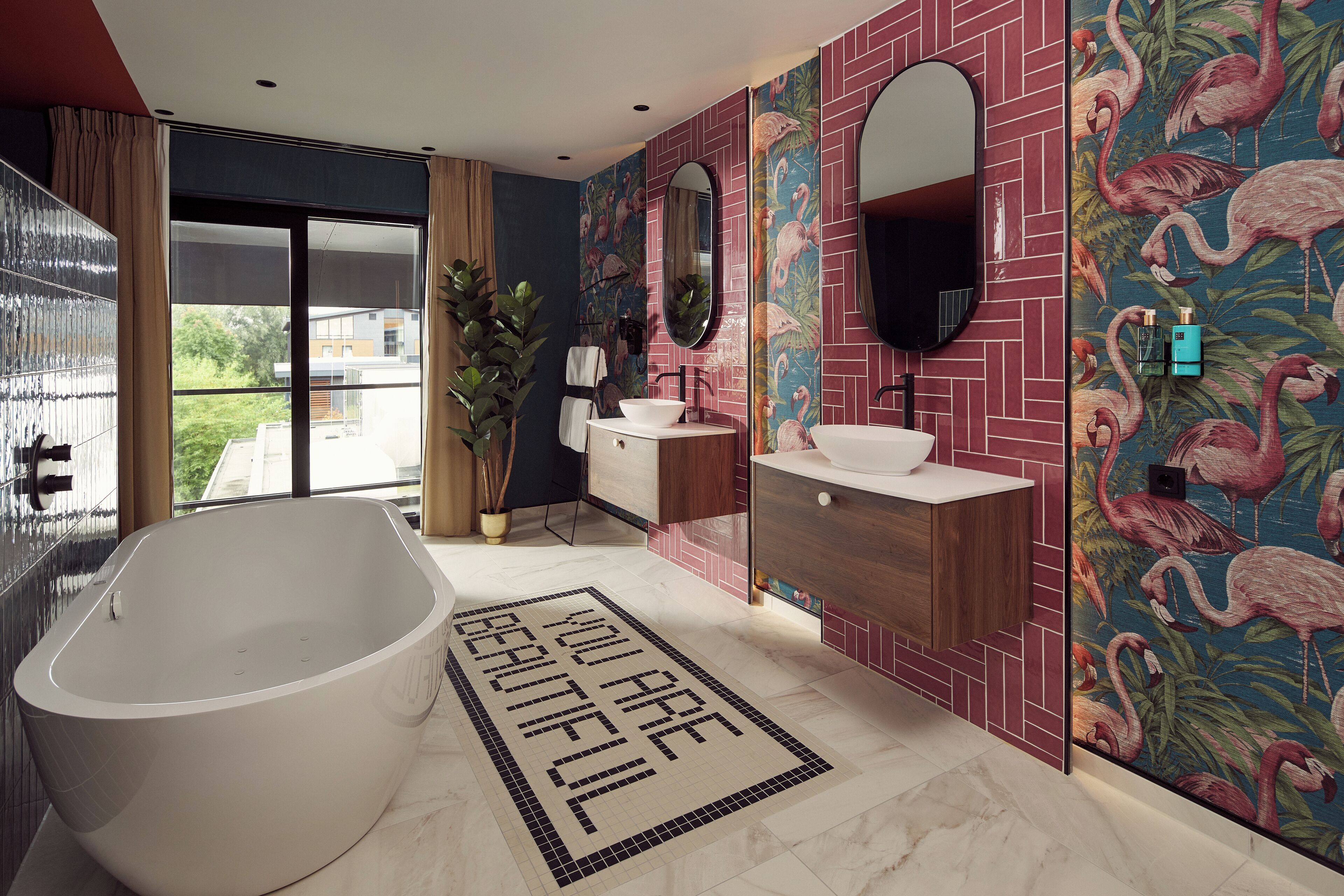 A modern bathroom with a freestanding bathtub, a vanity with a mirror, and a wall with a flamingo-themed tile design.