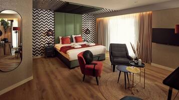 Une chambre d’hôtel moderne avec un grand lit, un coin salon comprenant un fauteuil et une petite table, ainsi qu’un miroir au mur.