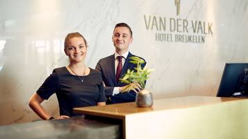 Een receptiebalie bij Van der Valk Hotel Breukelen, met een marmeren wand en een plant op de balie.