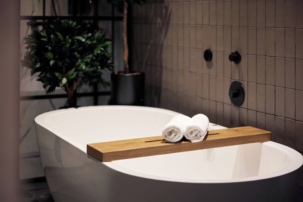 Un baño moderno con una bañera independiente, un estante de madera con toallas, una planta en maceta y un grifo de pared.