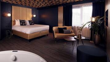 A modern hotel room with a large bed, a sofa, a small table, and a large potted plant.