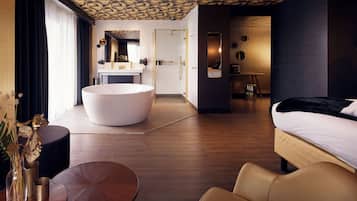 Habitació d'hotel moderna amb una banyera rodona gran, un llit, una taula rodona i un mirall.