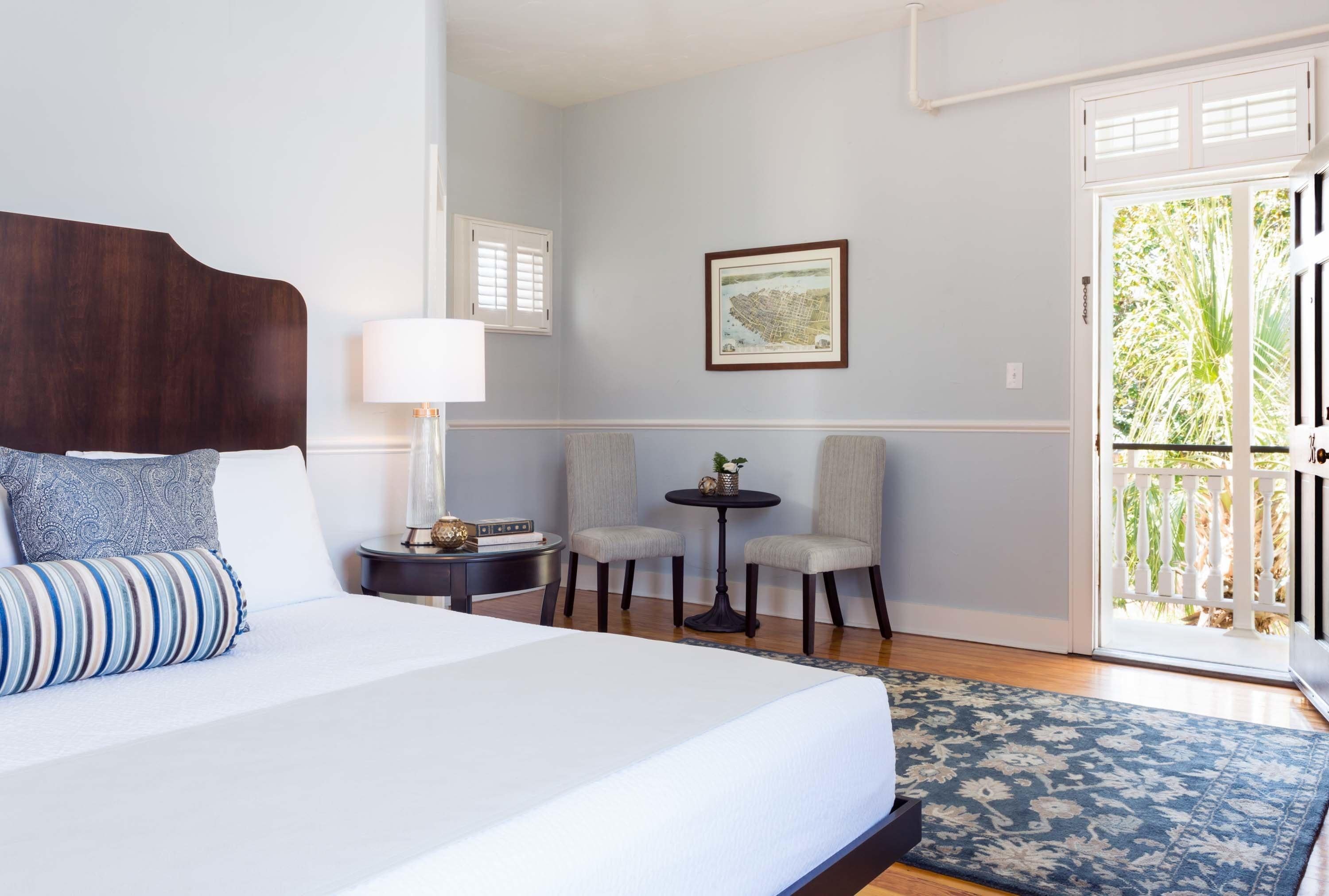 A hotel room with a large bed, two chairs, a small table, and a door leading to a balcony.