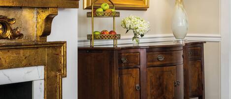 A room with a fireplace, a wooden cabinet with a vase and apples, and a painting on the wall.