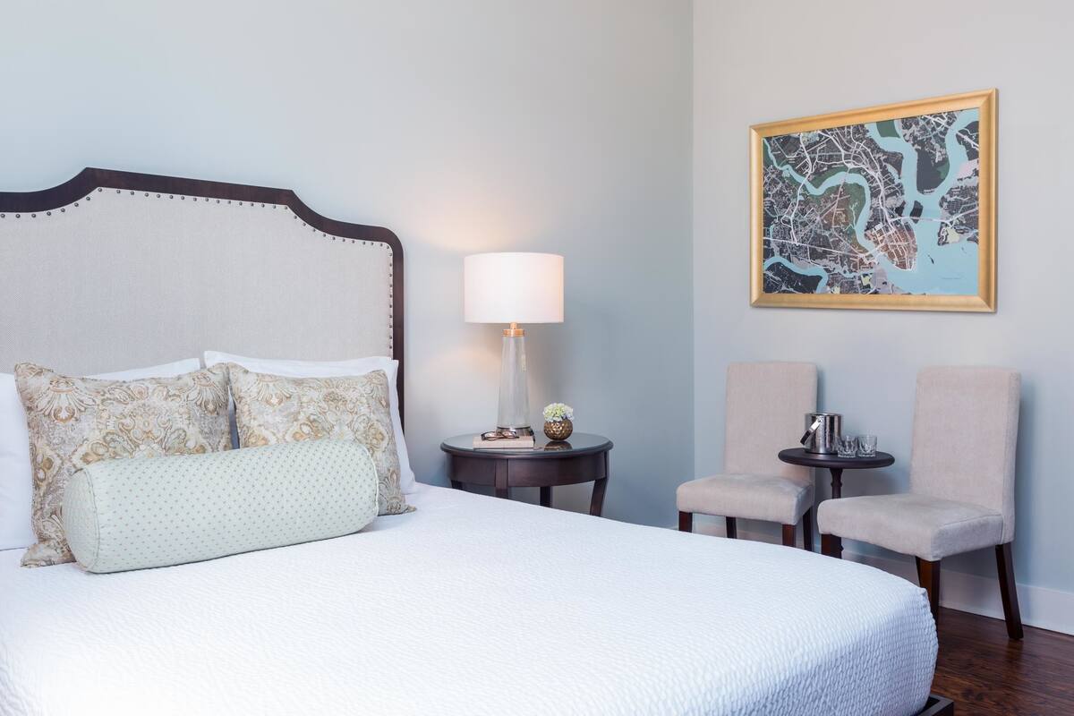 A neatly made bed with patterned pillows, a bedside lamp, and a framed map on the wall.