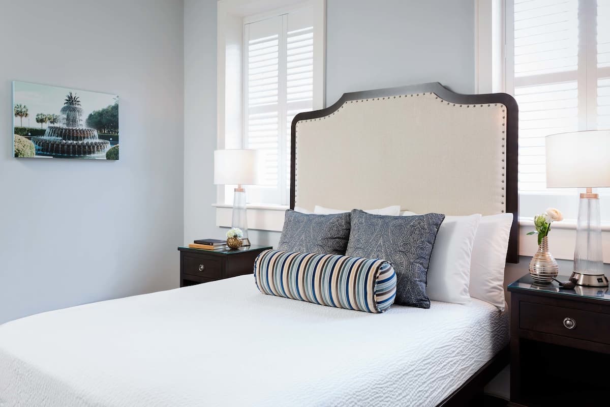 A neatly made bed with a striped pillow, a headboard with a decorative top, and a nightstand with a lamp and a vase.