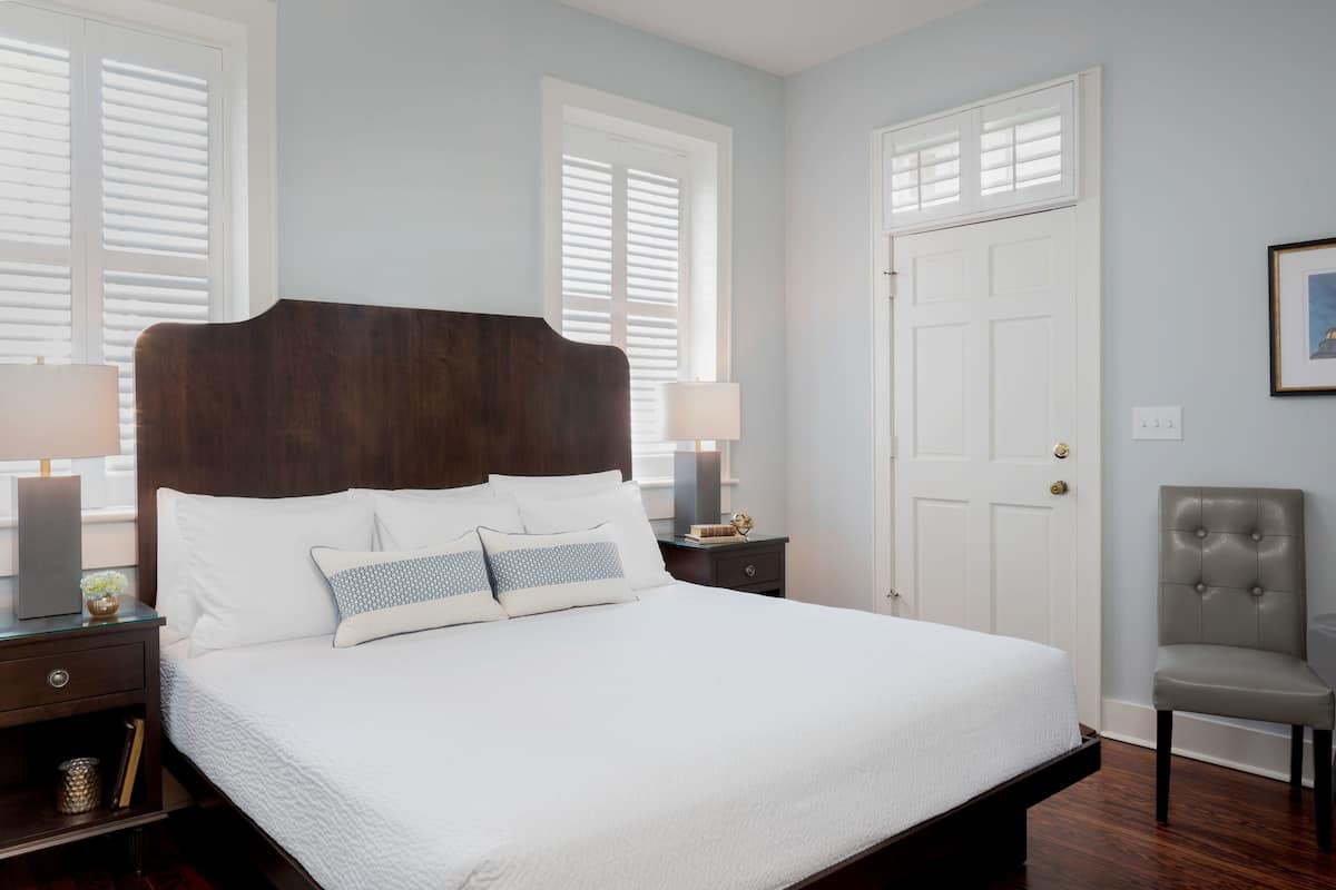A neatly made bed with a dark headboard, a bedside table with a lamp, and a chair.