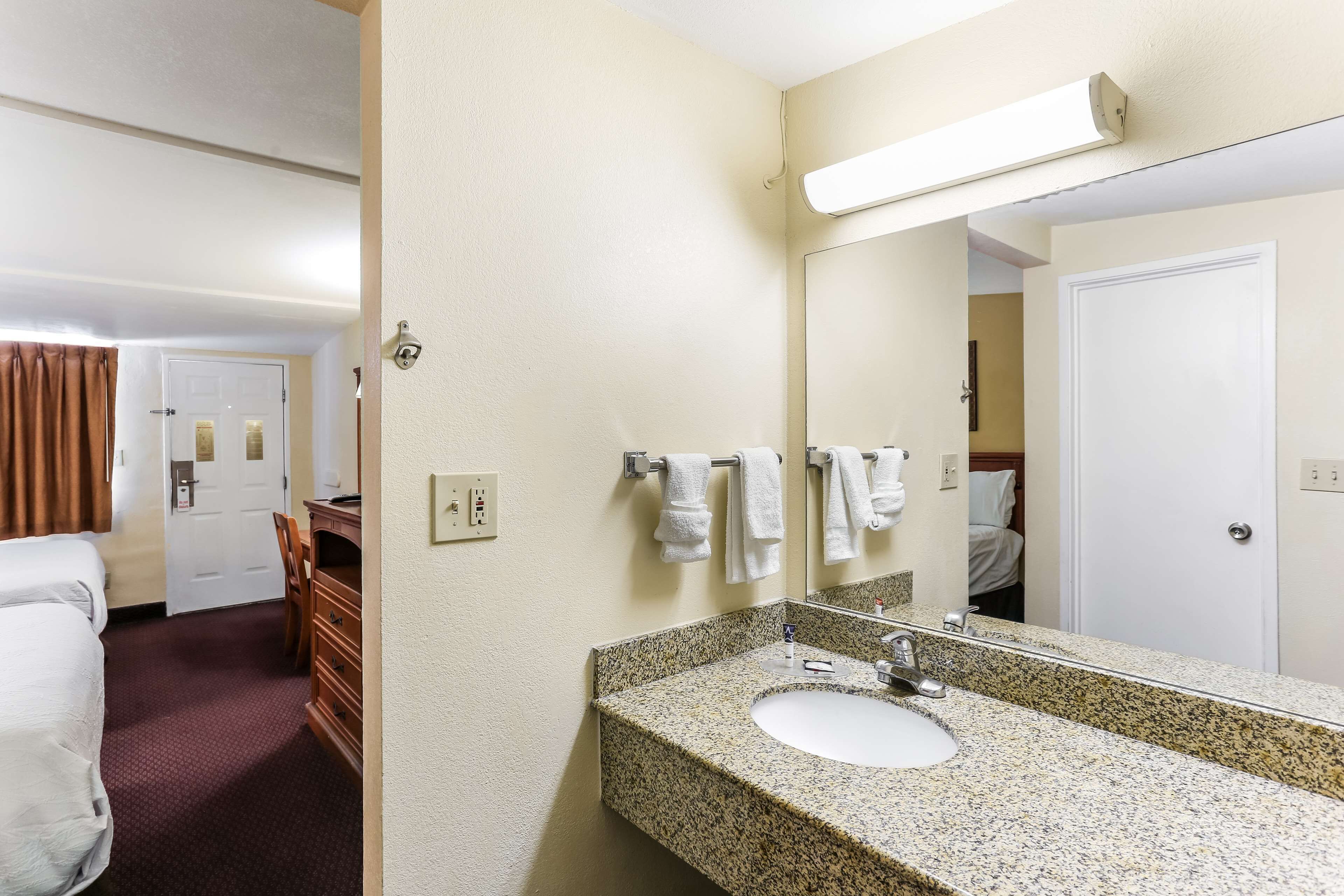 Baño de hotel con lavamanos de granito, un espejo y una puerta blanca.