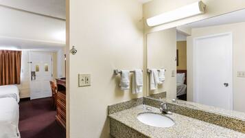 Baño de hotel con lavamanos de granito, un espejo y una puerta blanca.