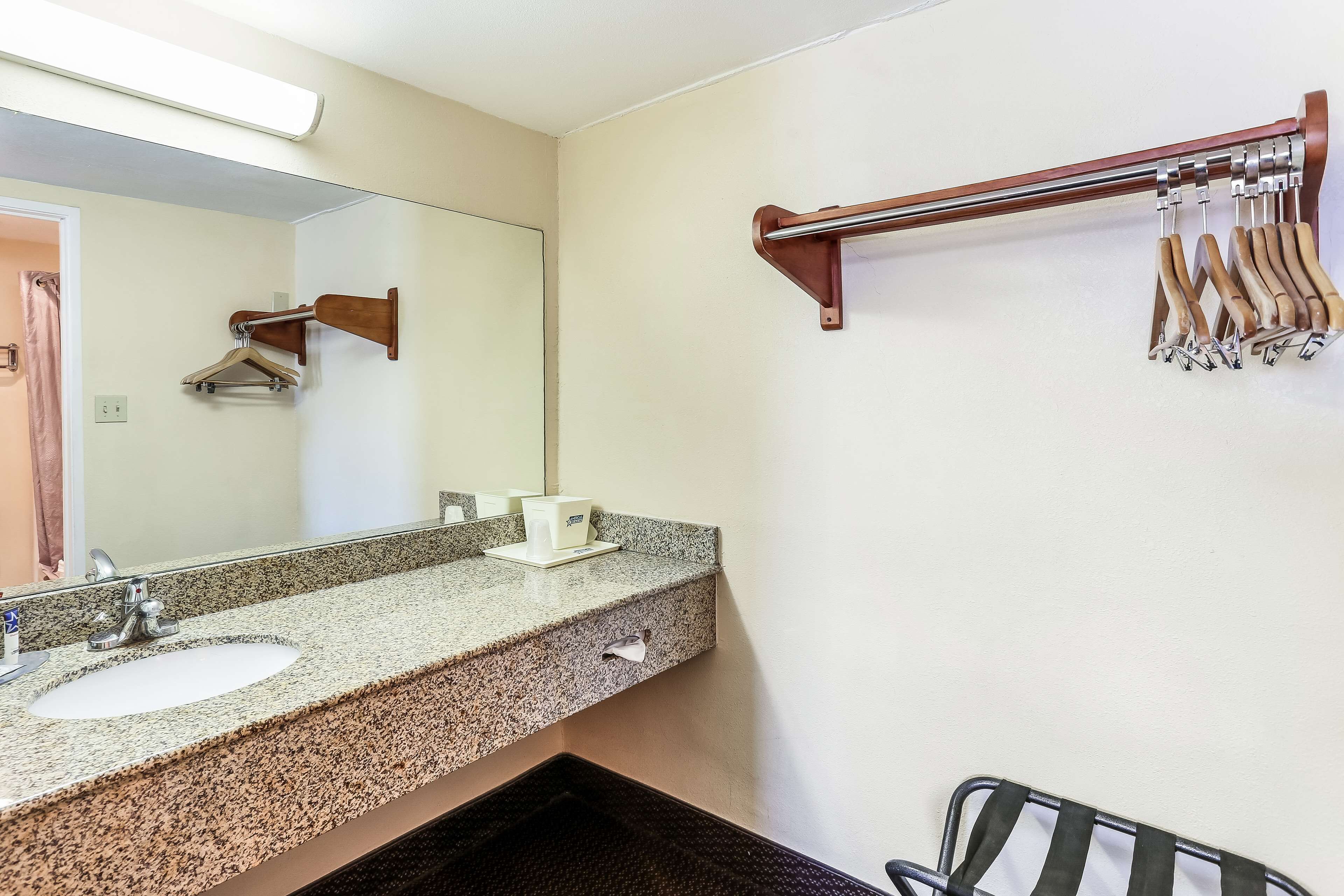 Un baño con lavamanos de encimera de granito, un espejo, toallero y barra para toallas.
