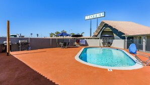 Um motel com piscina, área de estar externa e um céu azul límpido.