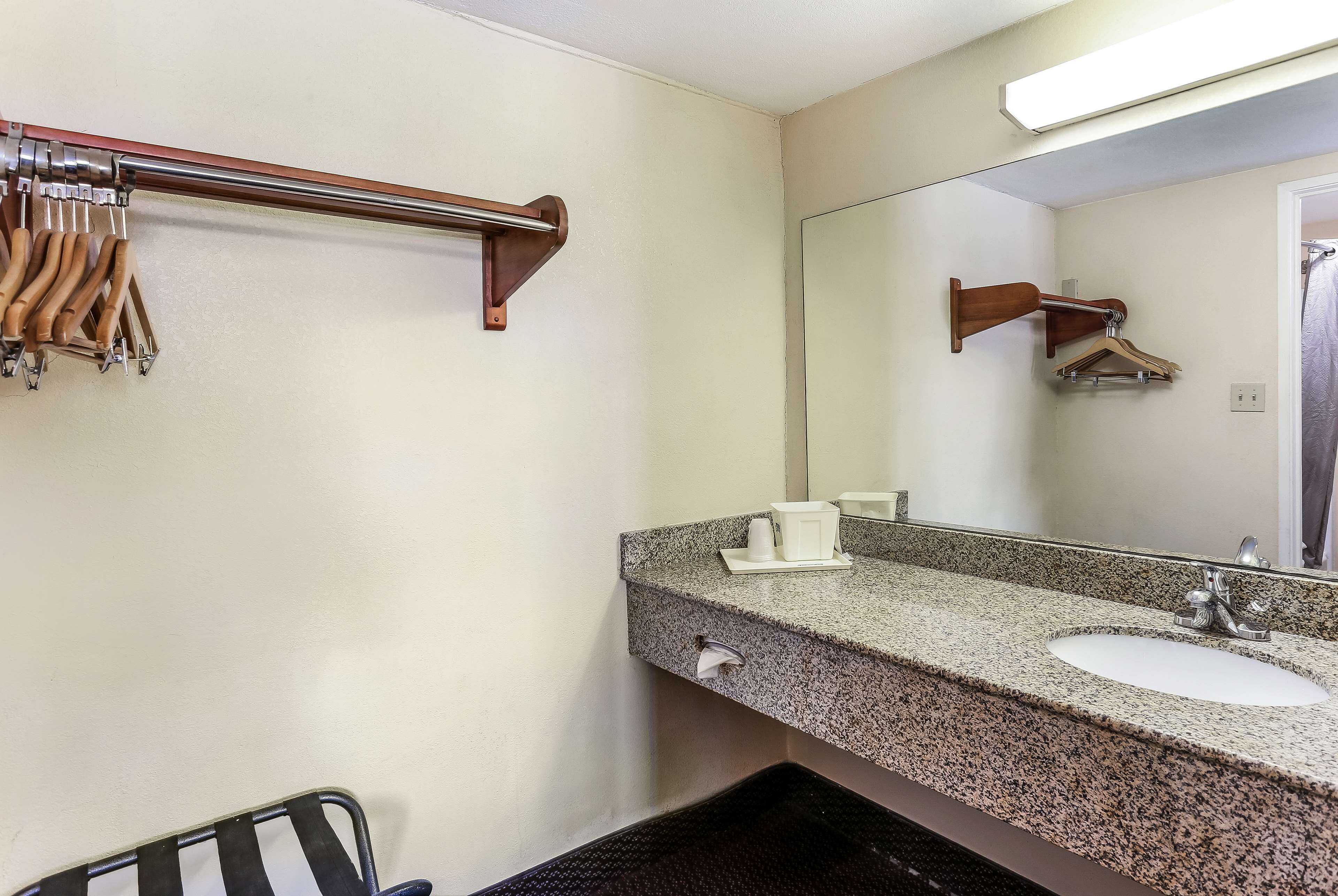 A bathroom with a granite countertop sink, a mirror, a towel rack, and a towel dispenser.