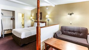 Quarto de hotel com cama, uma cadeira de madeira, sofá, mesa e banheiro com chuveiro e porta-toalhas.