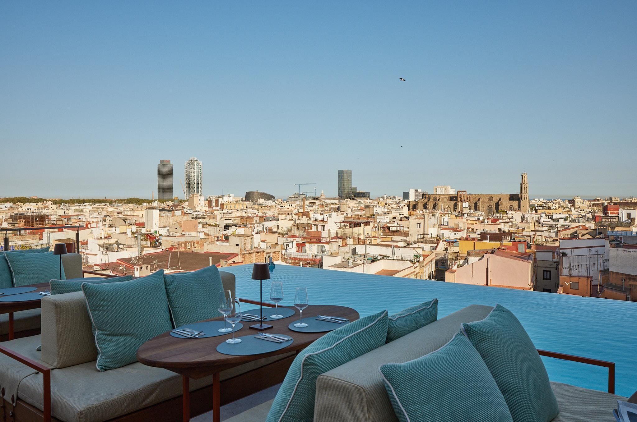 A rooftop terrace with a pool, seating area, and a view of a cityscape.