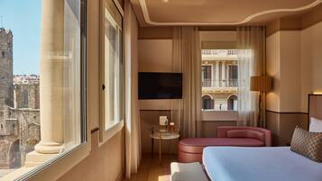 Habitació d'hotel amb un llit gran, un sofà rosa, una taula petita amb una làmpada i una televisió.