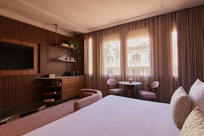 Ett hotellrum med en stor säng, en tv som är monterad på väggen, en väggpanel i trä, ett litet runt bord med stolar och utsikt från balkongen.