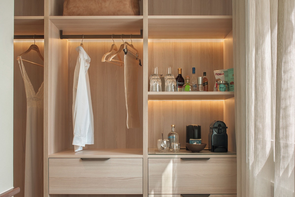 A wooden closet with hanging space for clothes, shelves for storage, and a countertop with personal items.