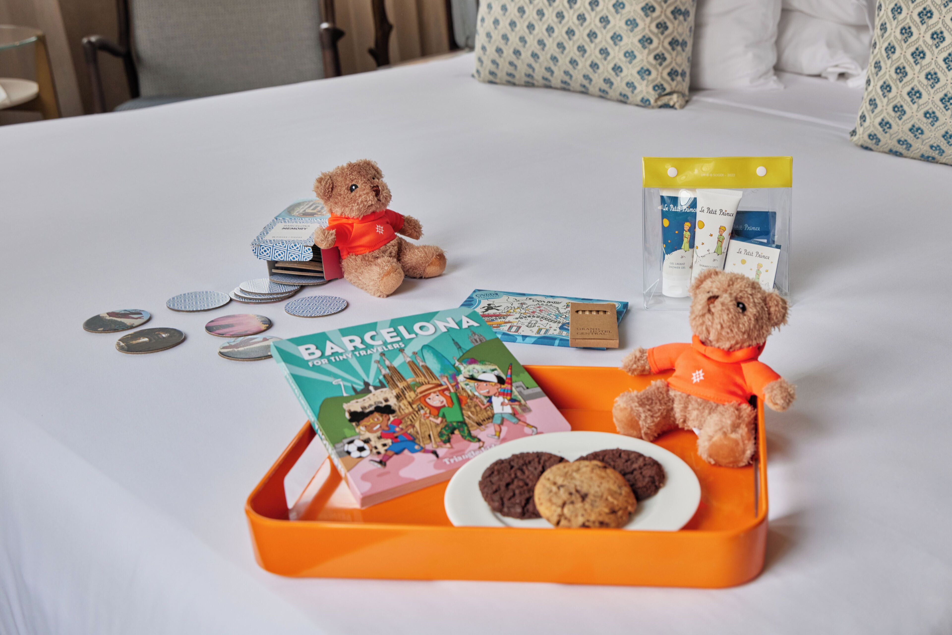 Una bandeja ordenada con un libro, galletas y un oso de peluche sobre la cama.