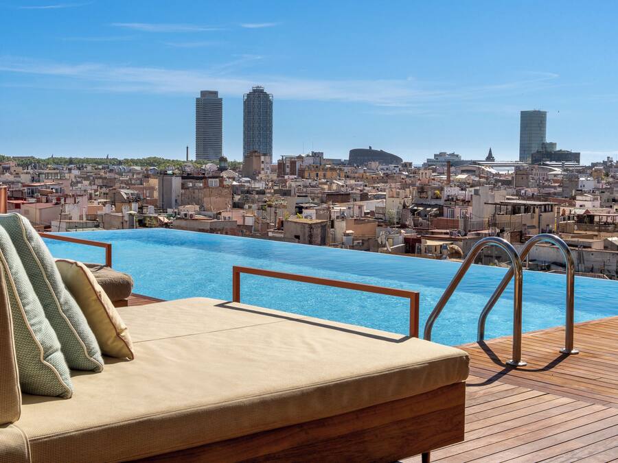 Une piscine sur le toit avec vue sur la ville, un espace détente avec des coussins et une terrasse en bois.