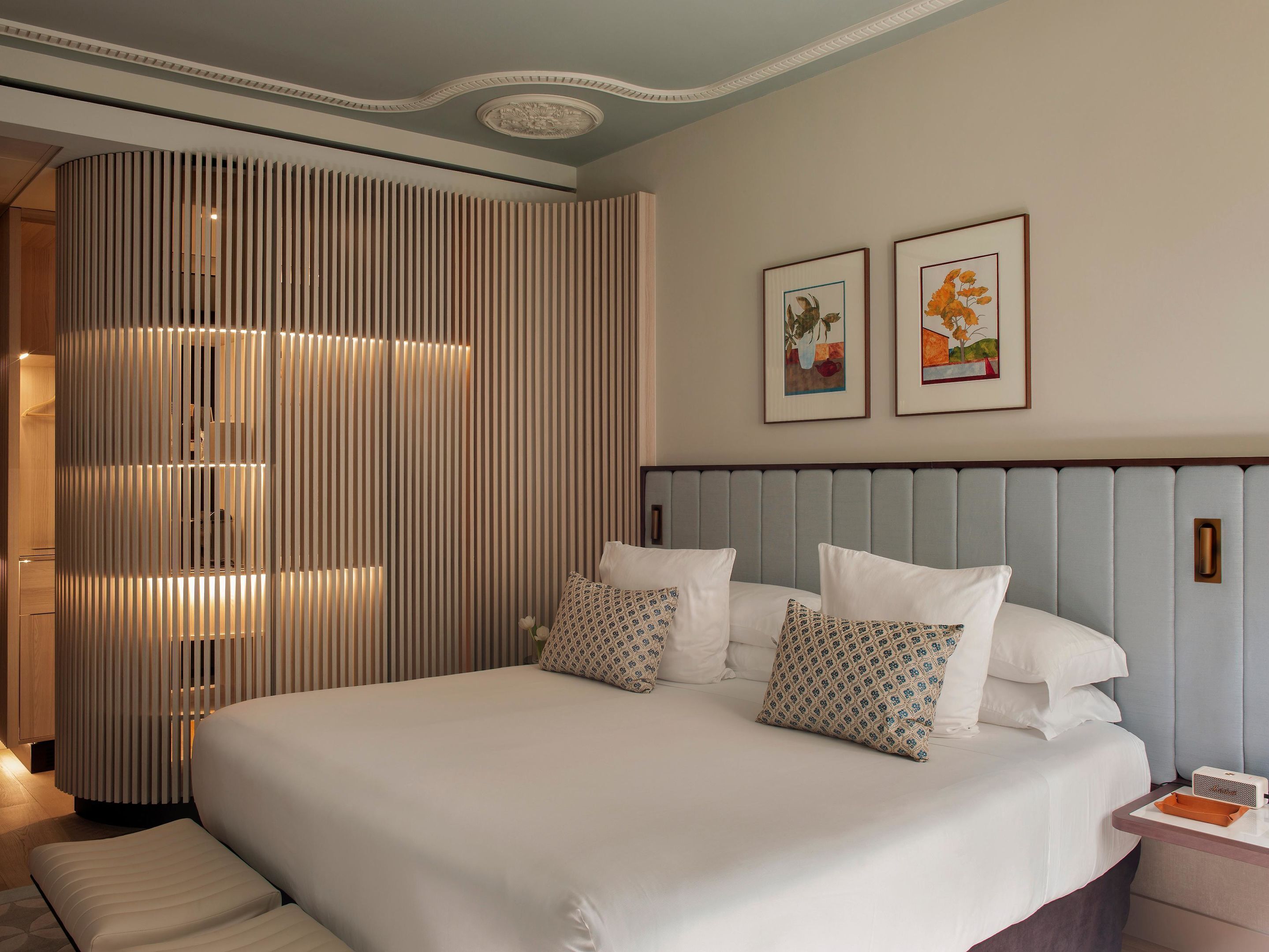 A hotel room with a large bed, a bedside table with a lamp, and two framed pictures on the wall.