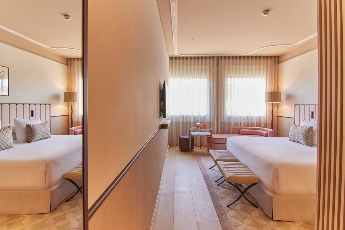 A hotel room with two beds, a small round table, a sofa, and a mirror.