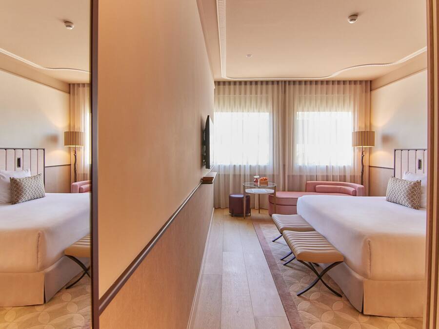 A hotel room with two beds, a small round table, a sofa, and a mirror.