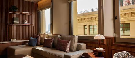 Una sala de estar moderna con un sofá, una mesa de centro y una lámpara. Se ve una ventana con vistas a un edificio.