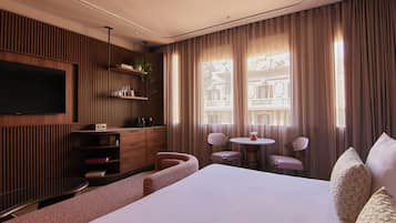 A hotel room with a bed, a TV, a desk, a chair, a small table, and a window with curtains.