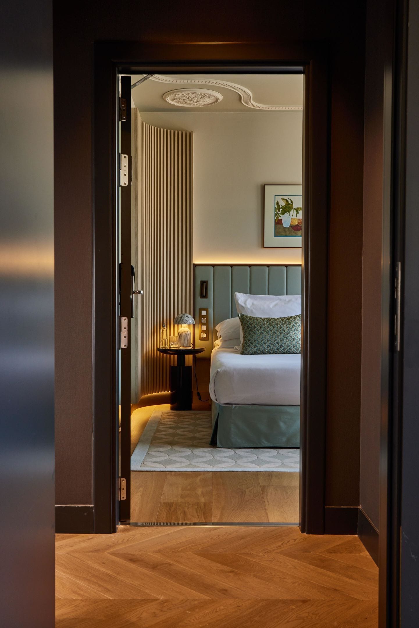 Una habitación de hotel con cama, mesita de noche, lámpara y un cuadro en la pared.