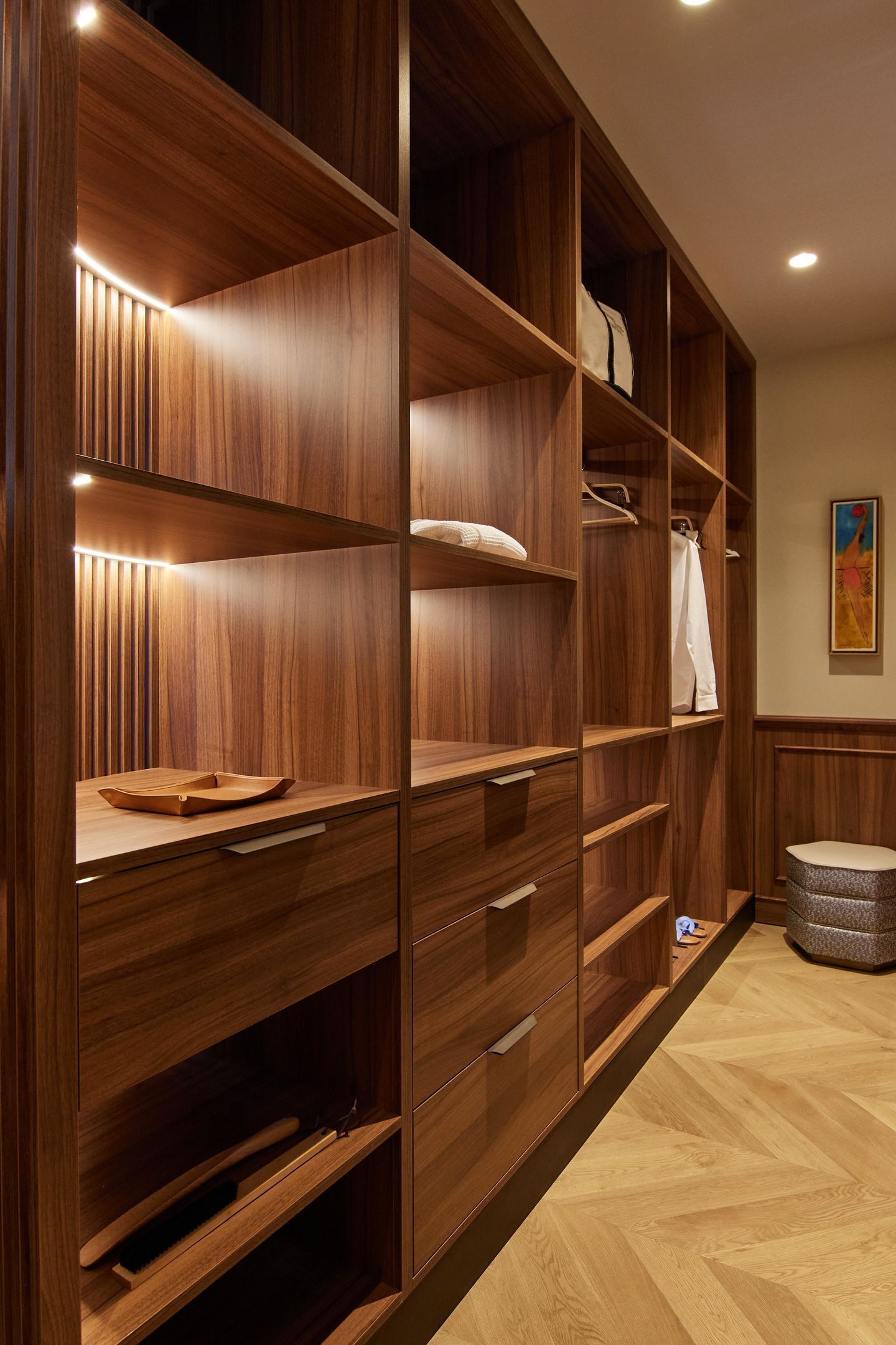 Un armario vestidor de madera con estantes y cajones múltiples, iluminado por luces debajo de los armarios.