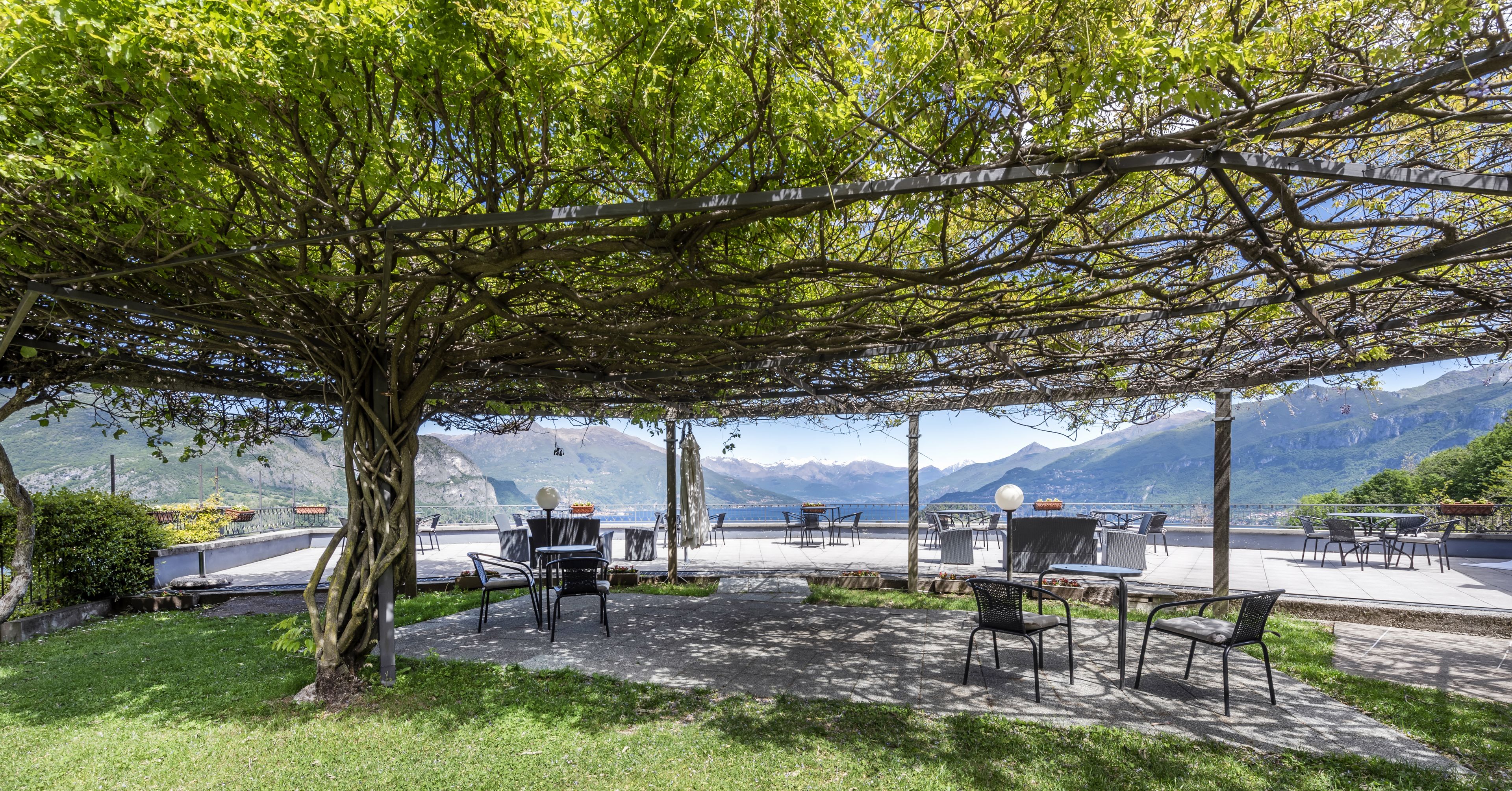 Un espace extérieur aménagé avec des tables et des chaises, entouré d’arbres et offrant une vue sur un plan d’eau, avec des montagnes en arrière-plan.