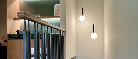 Una escalera con barandilla de metal, un accesorio de iluminación y una cocina al fondo.