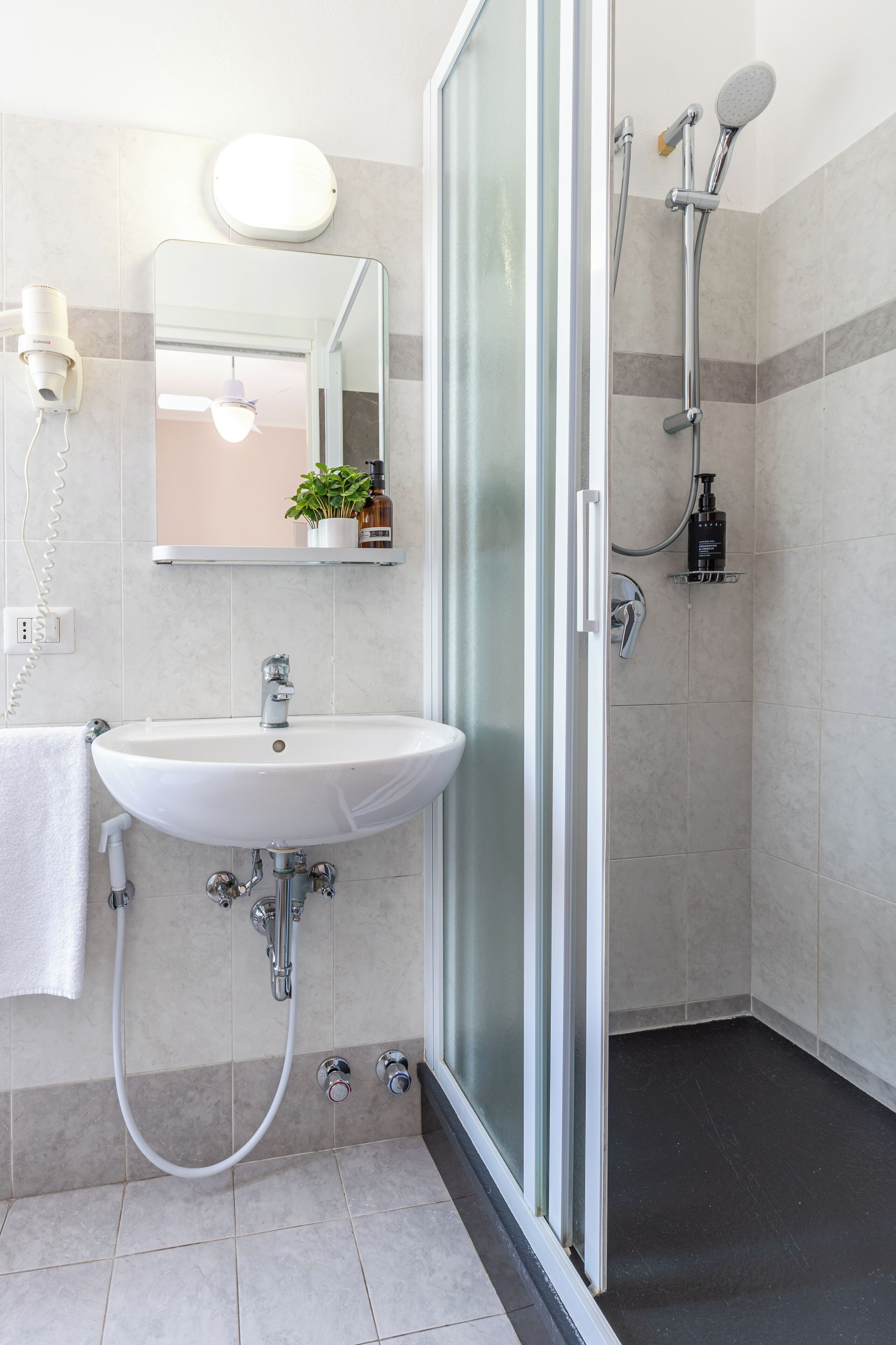 Et moderne badeværelse med en brusekabine i glas, en hvid vask og et spejl over vasken.