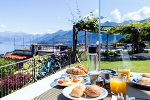 A table with breakfast items, a bicycle, and a scenic mountain view. - Il Perlo Panorama (Bellagio)