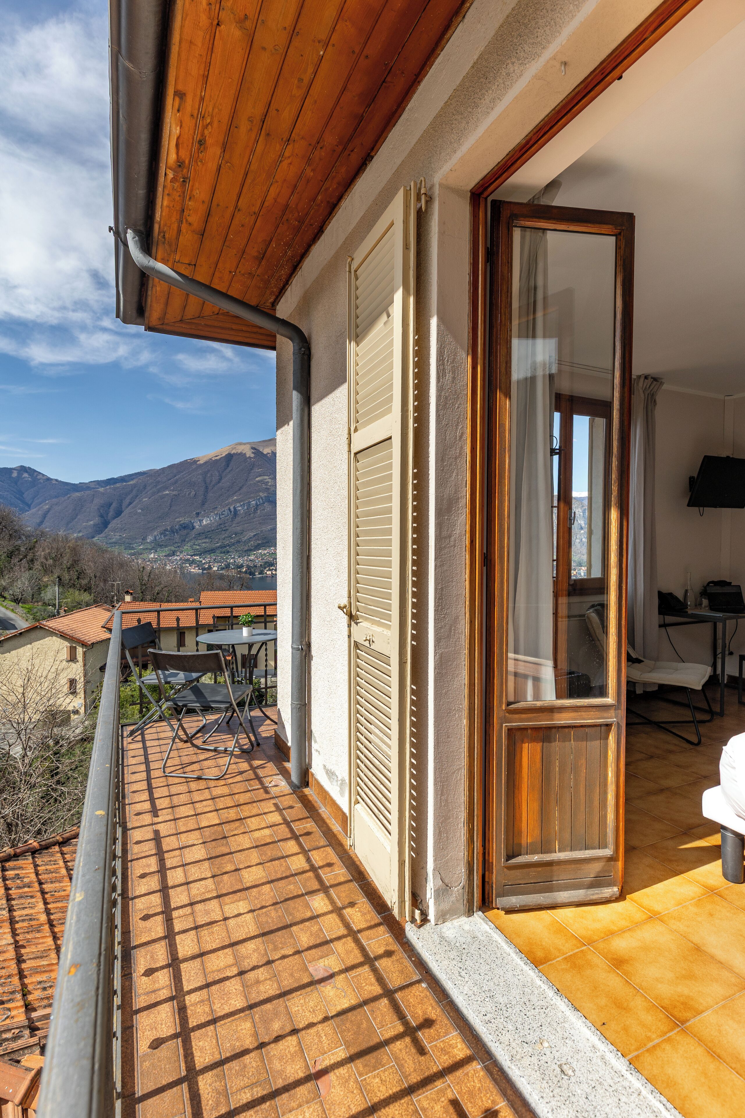 Varanda com vista para montanhas, porta de madeira e mesa com cadeiras.