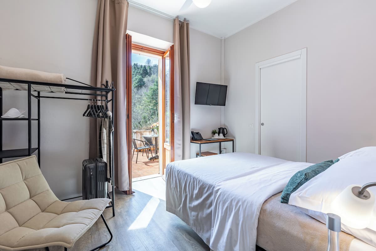 A hotel room with a bed, a chair, a desk with a computer, a TV, and a view of the outdoors.