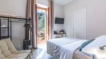 Ein Hotelzimmer mit einem Bett, einem Sessel, einem Schreibtisch mit Computer, einem Fernseher und Blick ins Freie.