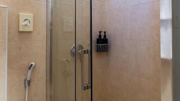 Cabina doccia in vetro con soffione a mano, miscelatore a muro e dispenser di sapone da parete.
