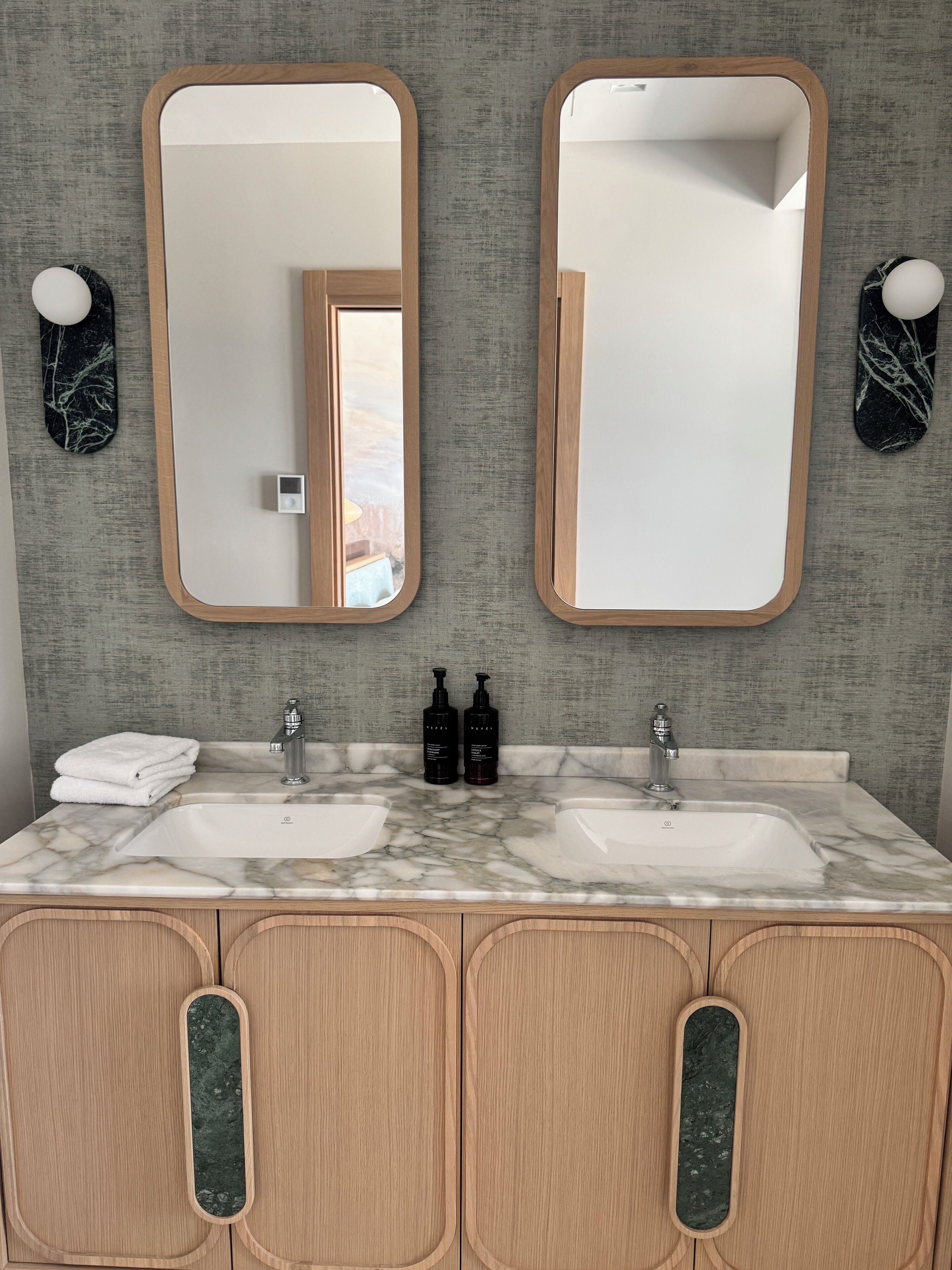Une salle de bain avec deux lavabos, des meubles en bois, des plans de travail en marbre et deux miroirs fixés au mur.