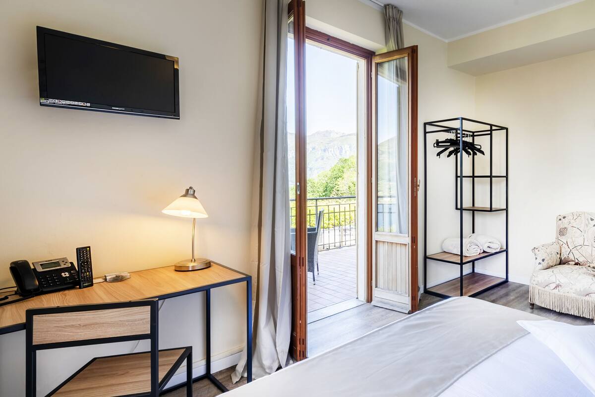A hotel room with a bed, a desk with a lamp, a chair, a TV, and a view of the outdoors.