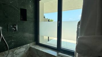 Un bagno moderno con una grande vasca, una doccetta e vista sul mare tramite una porta scorrevole.